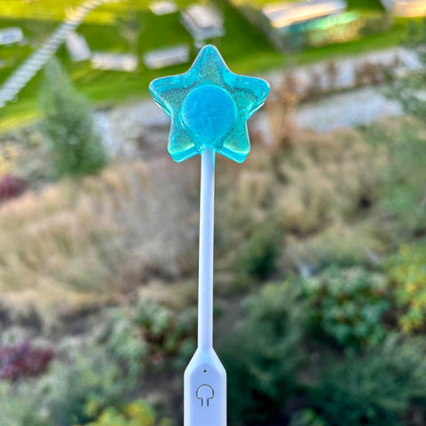 Star-shaped blue lollipop on a white stick with a blurred natural background